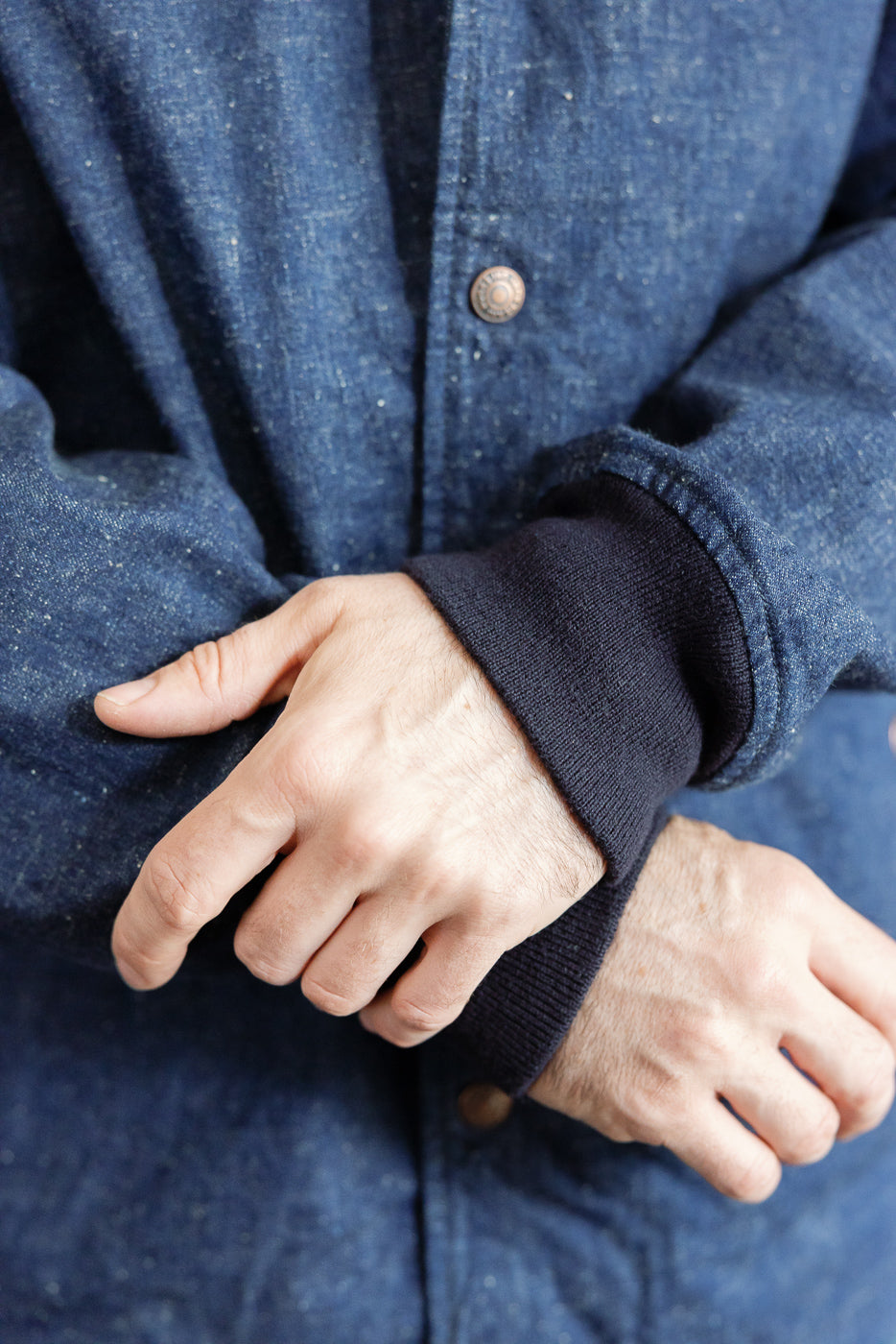 Close-up of male model's wrist showing navy ribbed cuff and button detail on denim shirt