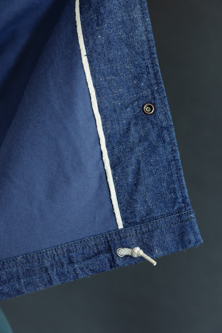 Close-up of denim jacket sleeve, front view, showing button, white stripe, and drawstring hem detail