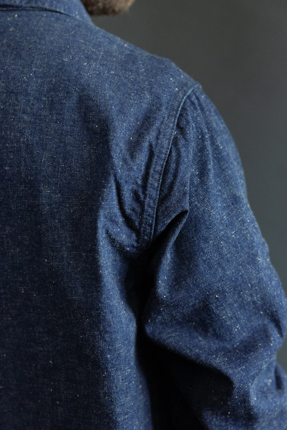 Close-up of male model's back shoulder, showcasing denim shirt texture and sleeve detail