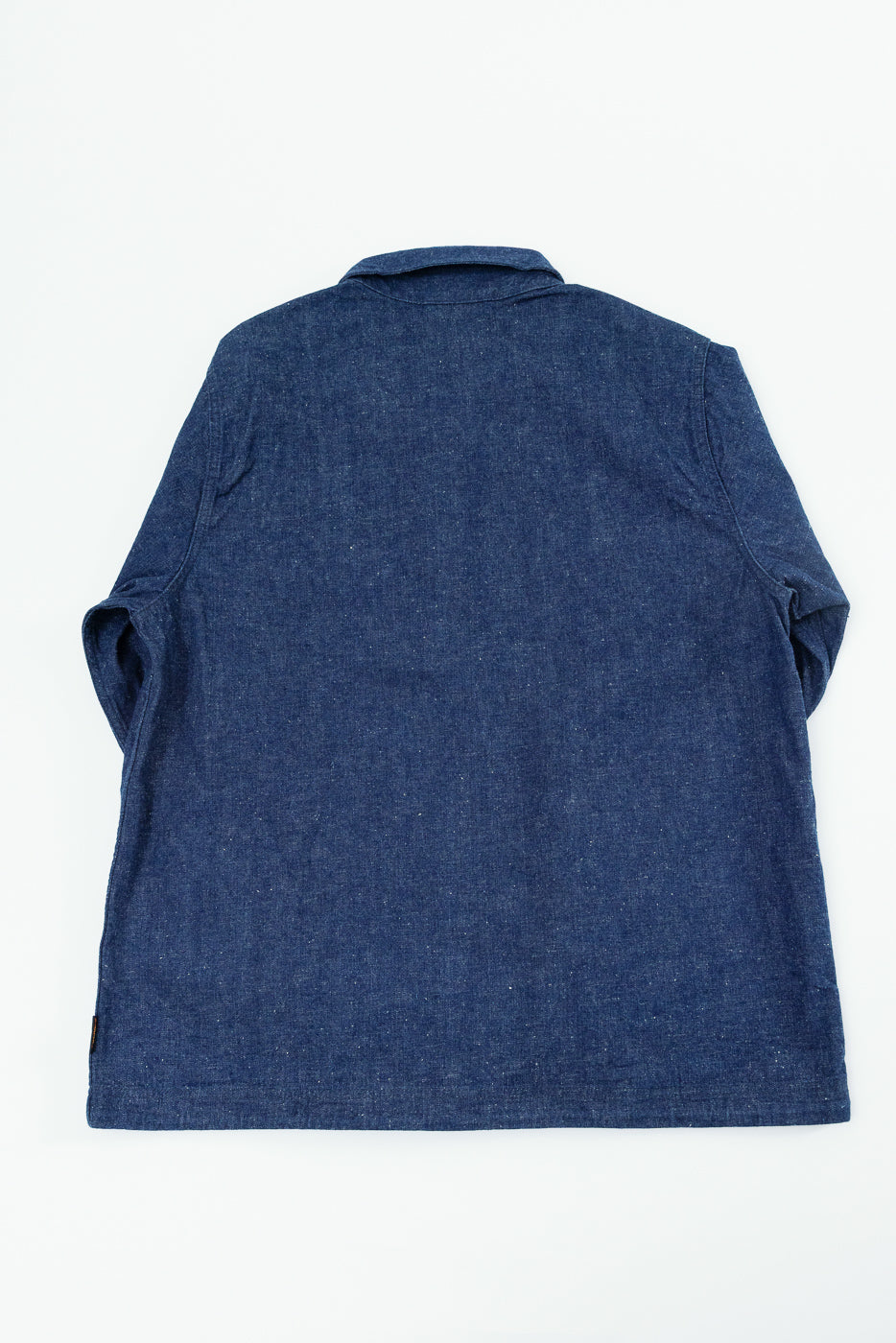 Back view of dark blue denim shirt, flat lay, showing collar, sleeve cuffs, and hem with tag detail