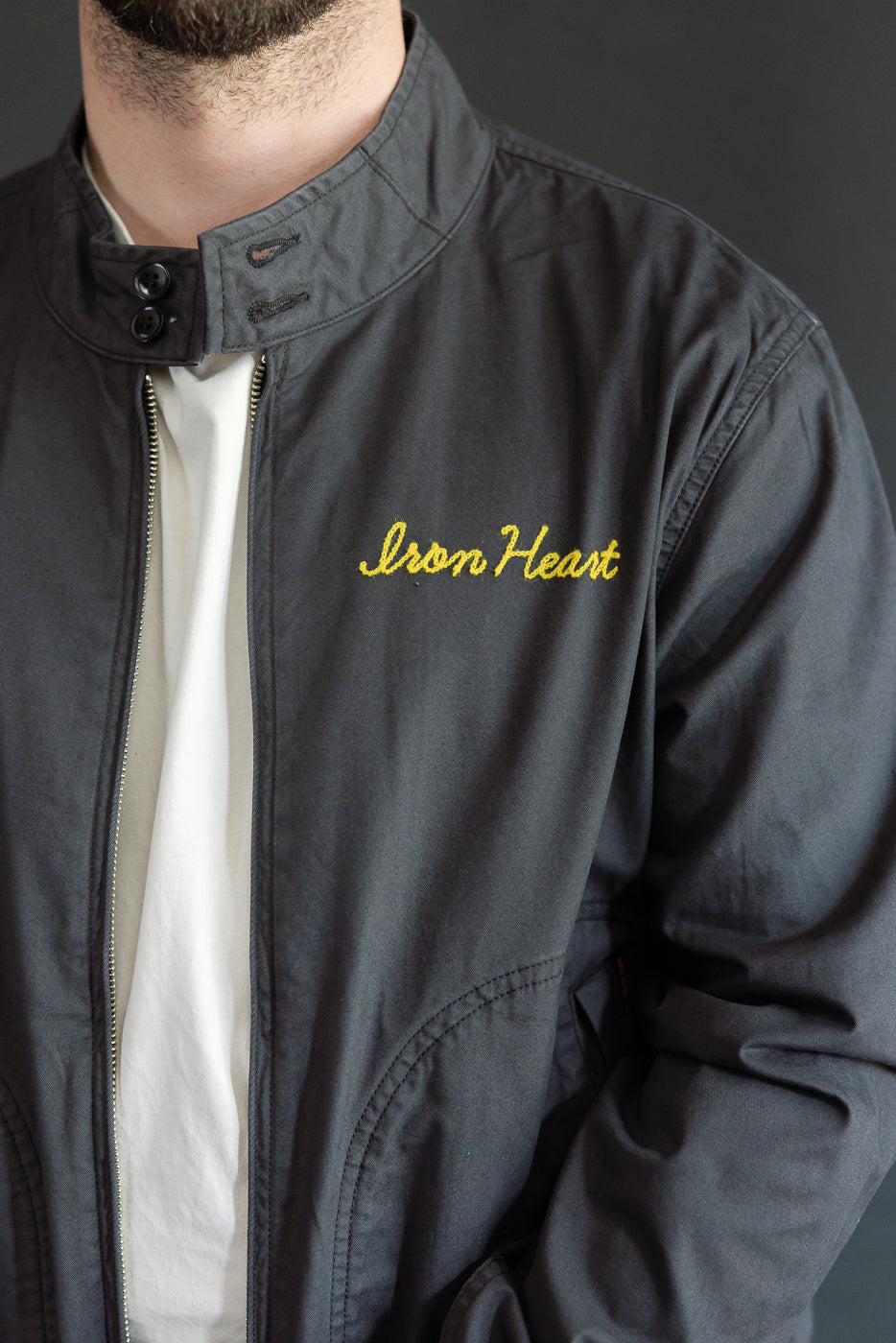 Close-up front view of male model in dark jacket with 'Iron Heart' embroidery, showing collar and zipper details.