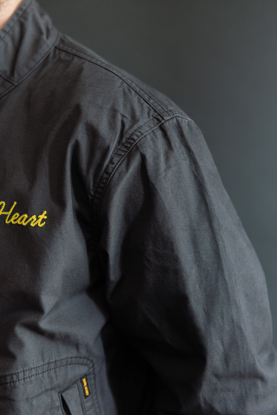 Close-up of black jacket front, yellow 'Heart' embroidery, male model 5'9