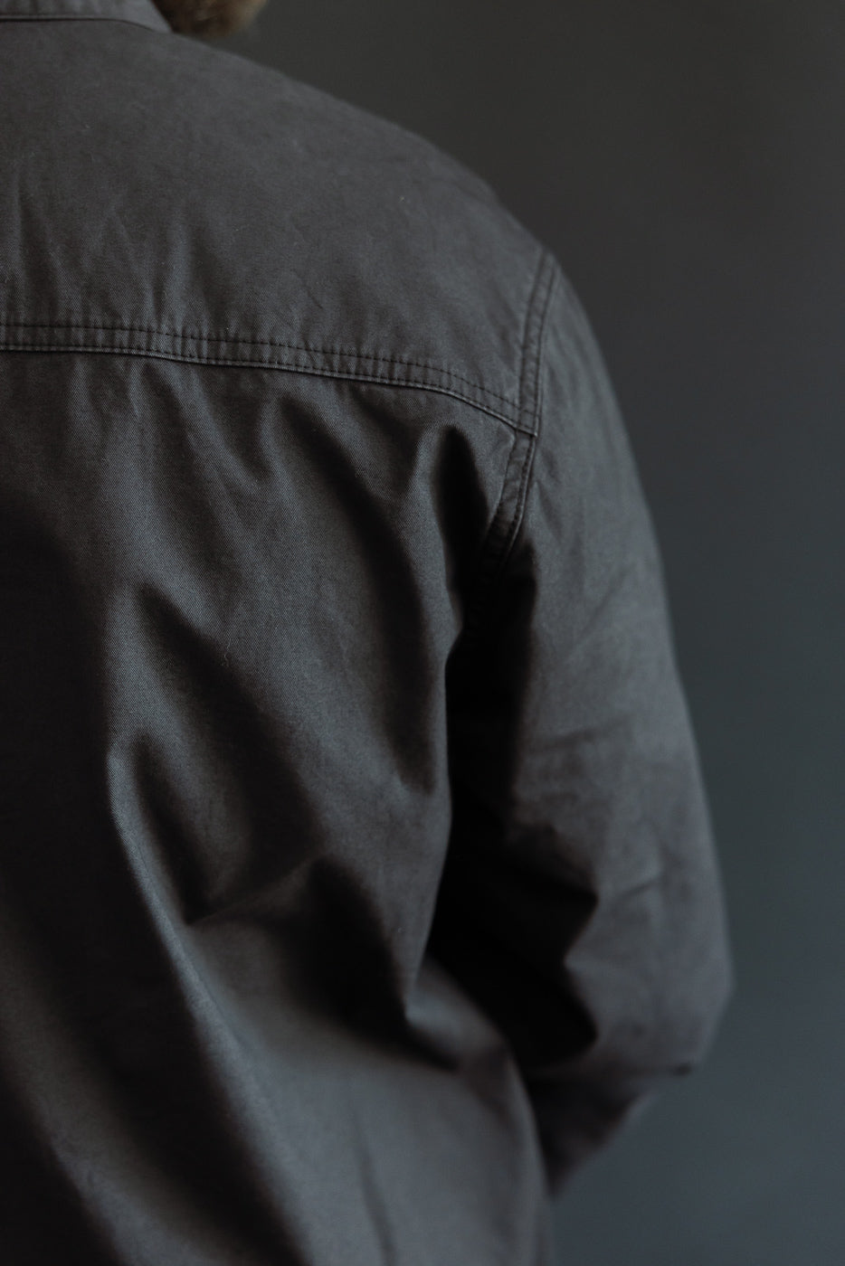 Back view close-up of dark gray shirt on male model, showcasing fabric texture and shoulder seam detail.
