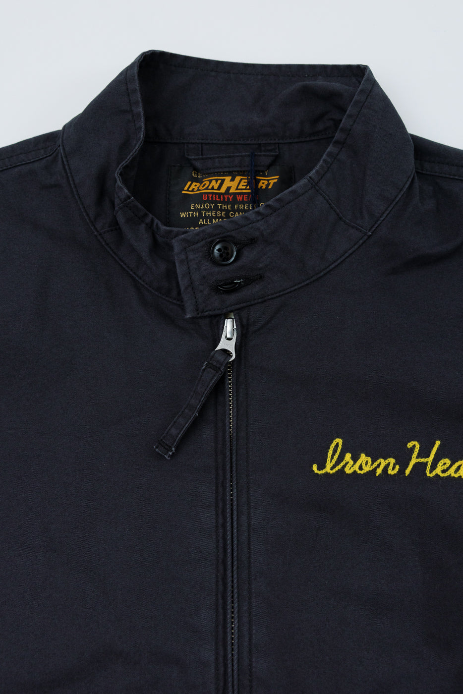 Close-up front view of black Iron Heart jacket, showing collar, zipper, and yellow embroidery detail.