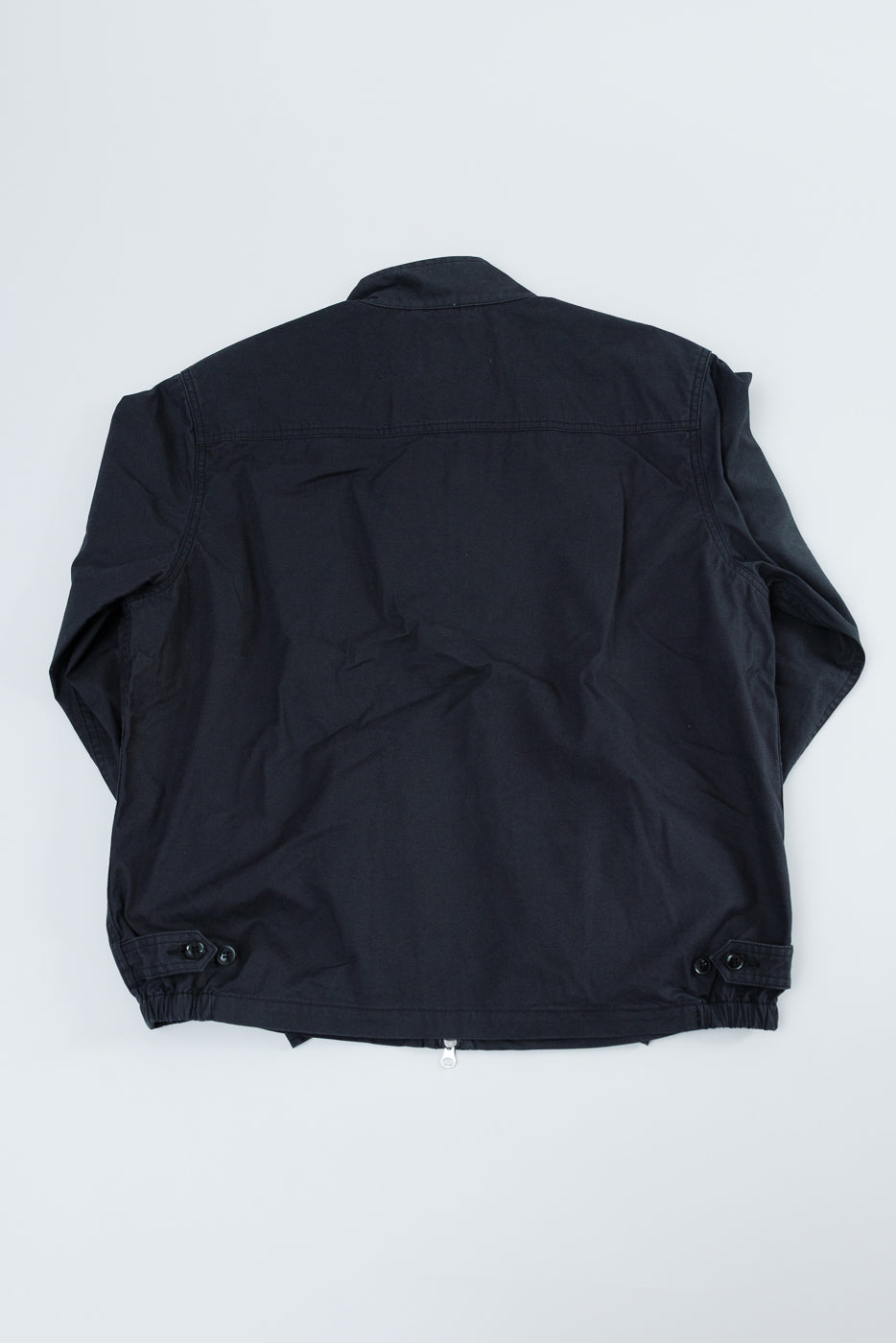 Back view of black jacket with buttoned cuffs and zipper hem, flat lay