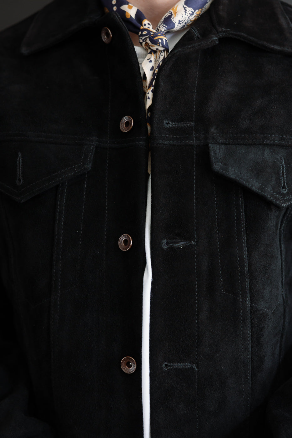Close-up front view of black suede jacket with snap buttons, chest pockets, and patterned neck scarf on male model.