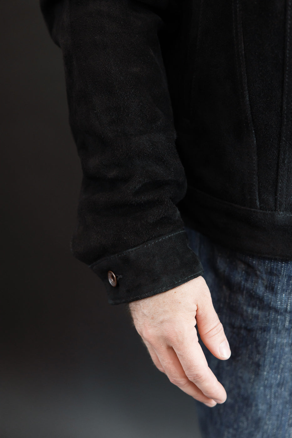 Close-up side view of male model's arm in black suede jacket, showing cuff button detail, 5'9