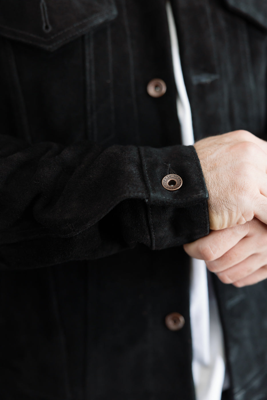Close-up front view of black suede jacket sleeve, showing button cuff detail, worn by male model