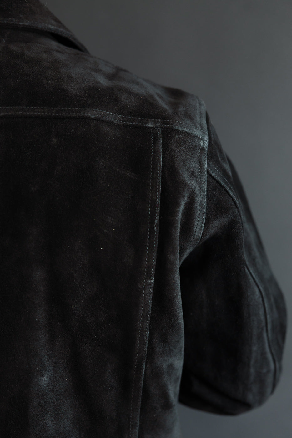 Close-up of dark suede jacket back shoulder, showing texture and stitching on male model, 5'9