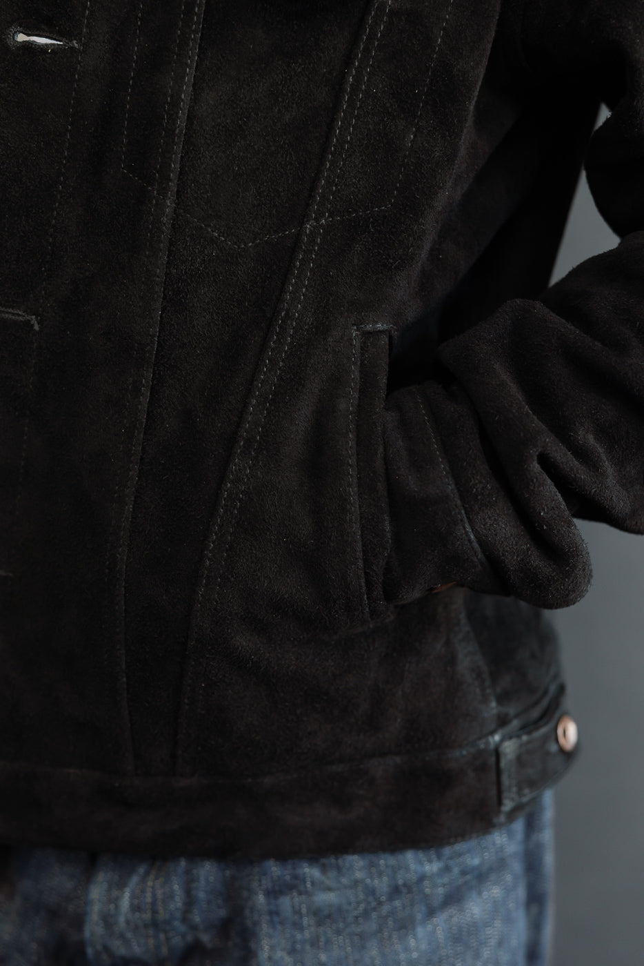 Close-up front view of black suede jacket, showing chest pocket, stitching, and hem detail on male model
