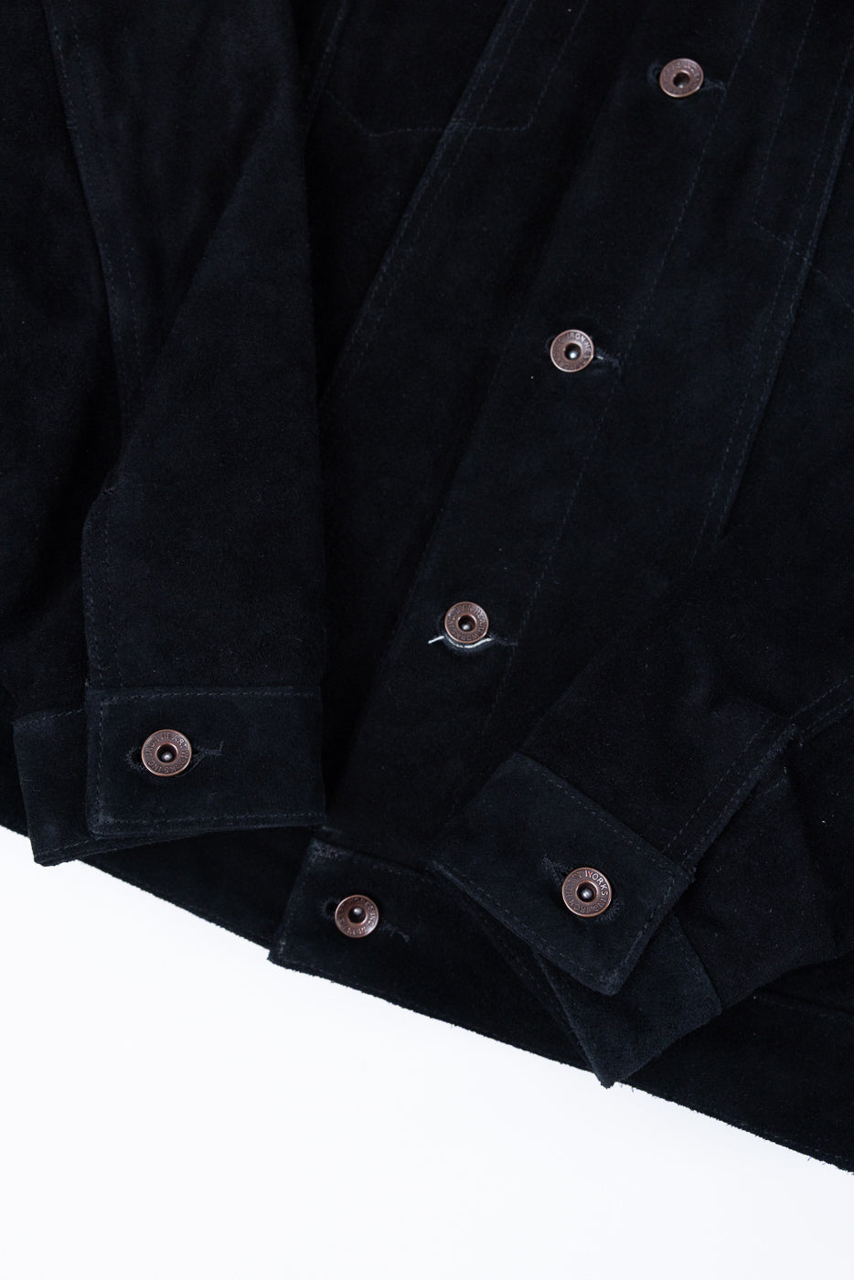 Close-up front view of black suede jacket with copper snap buttons and textured fabric detail