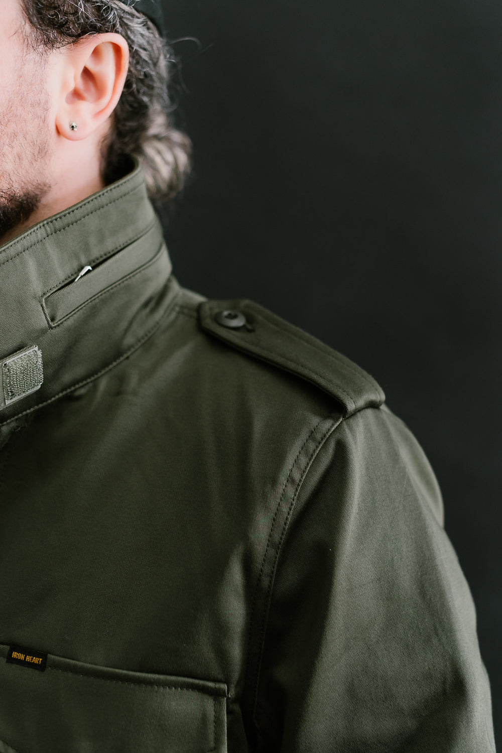 Close-up of Iron Heart olive M65 field jacket shoulder and collar details, male model, left side