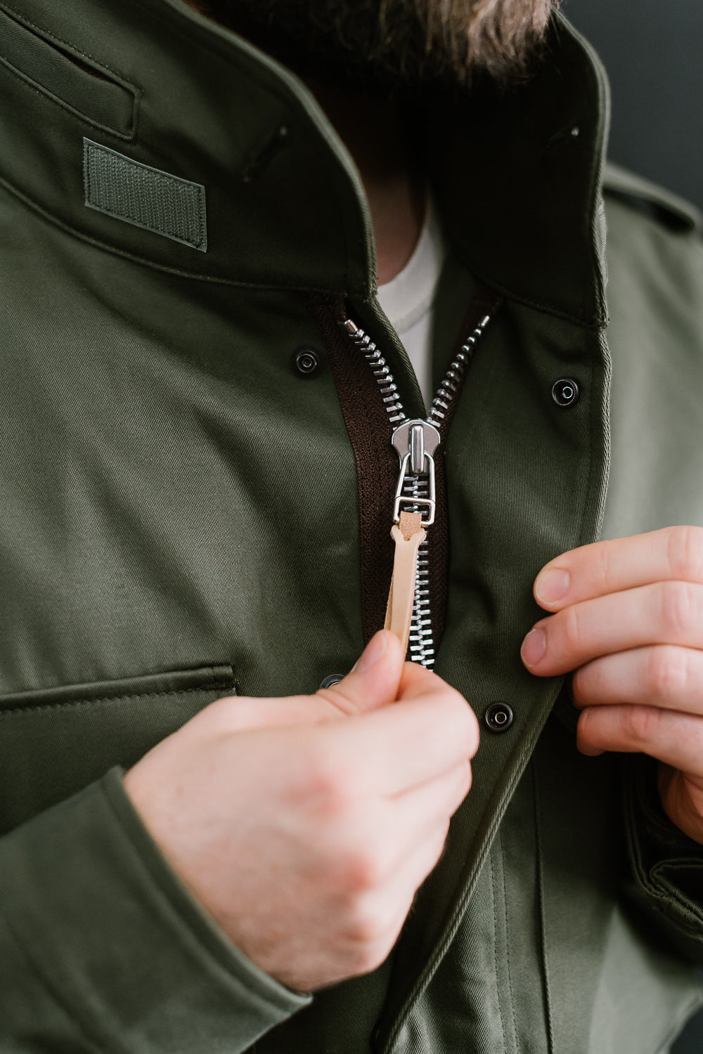 Close-up front view of Iron Heart olive M65 field jacket zipper, on male model 5'9