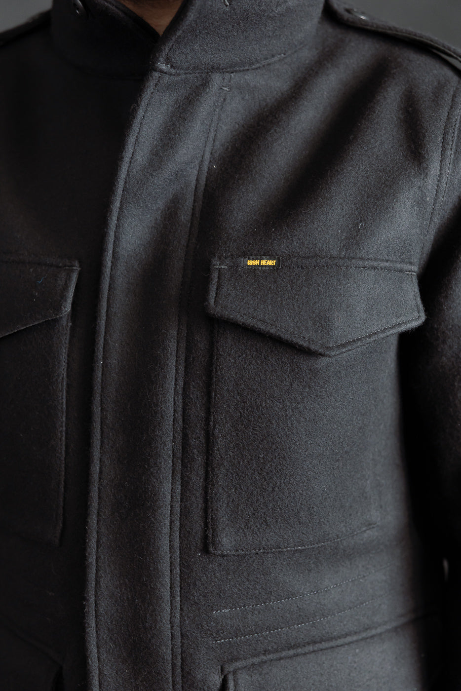 Close-up front view of Iron Heart M65 field jacket chest pockets, black melton wool, worn by male model 5'9
