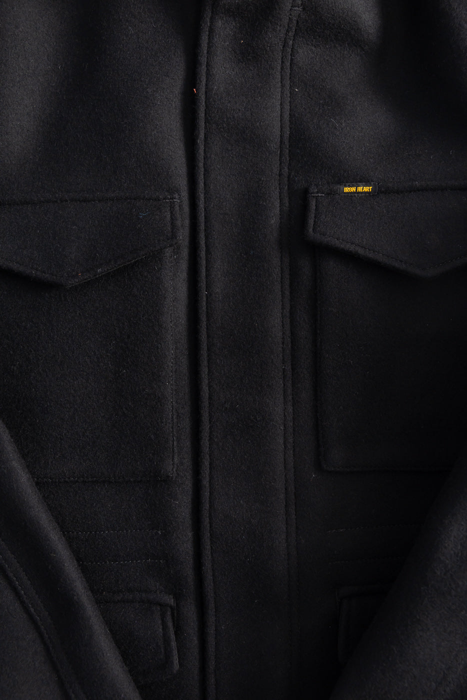 Close-up of Iron Heart IH-49 black melton wool M65 field jacket front chest pockets, fabric texture and gold brand tag detail.