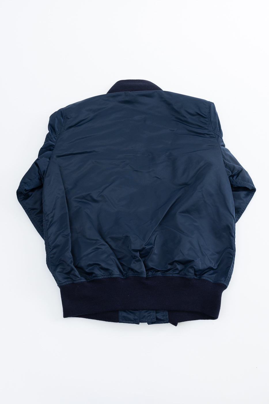 Flat lay of navy nylon jacket, back side view showing ribbed hem and collar detail.