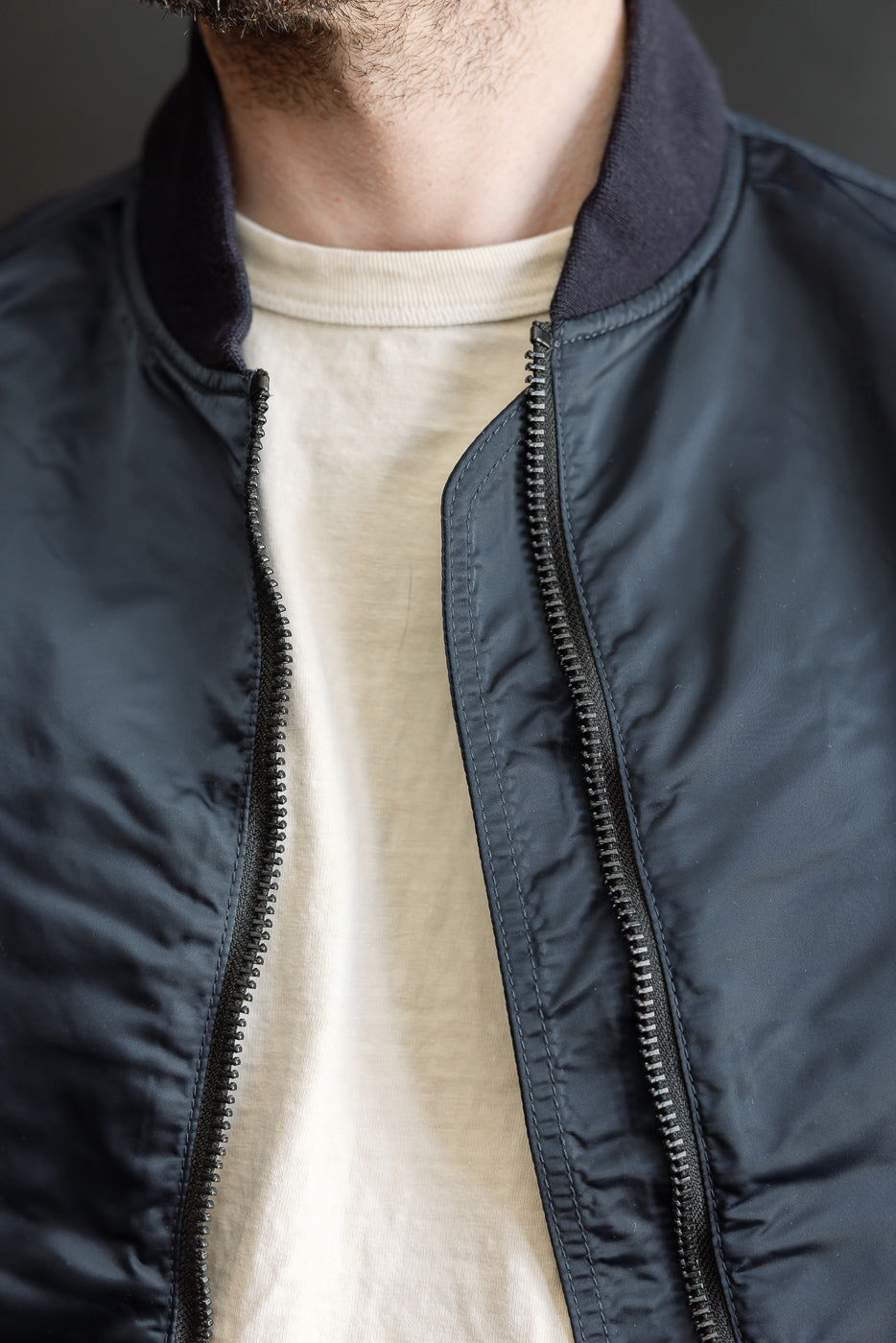 Close-up of navy nylon jacket front, zipper and ribbed collar, on male model 5'9