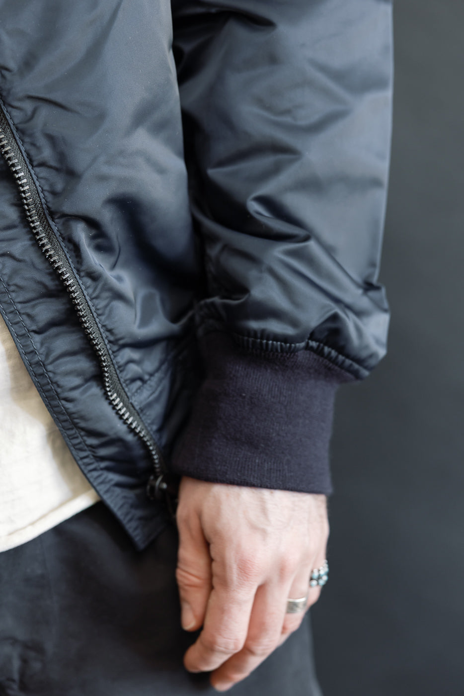 Close-up of men's navy nylon jacket sleeve and ribbed cuff, male model, front detail view.