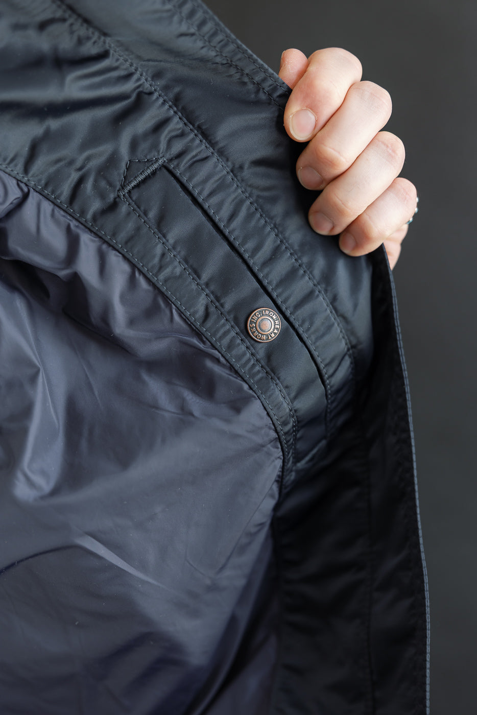 Close-up of interior pocket and snap button on navy nylon jacket, showing stitching detail.