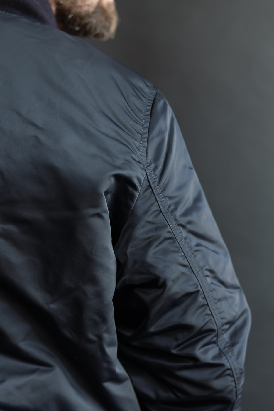 Close-up of men's navy nylon jacket back shoulder on male model, showing stitching detail