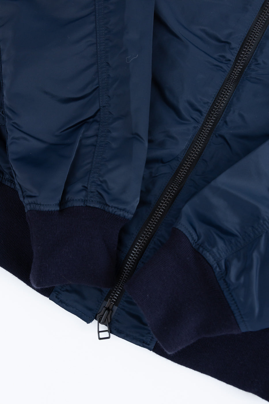 Close-up of navy nylon jacket front, showing zipper, ribbed cuffs, and hem details