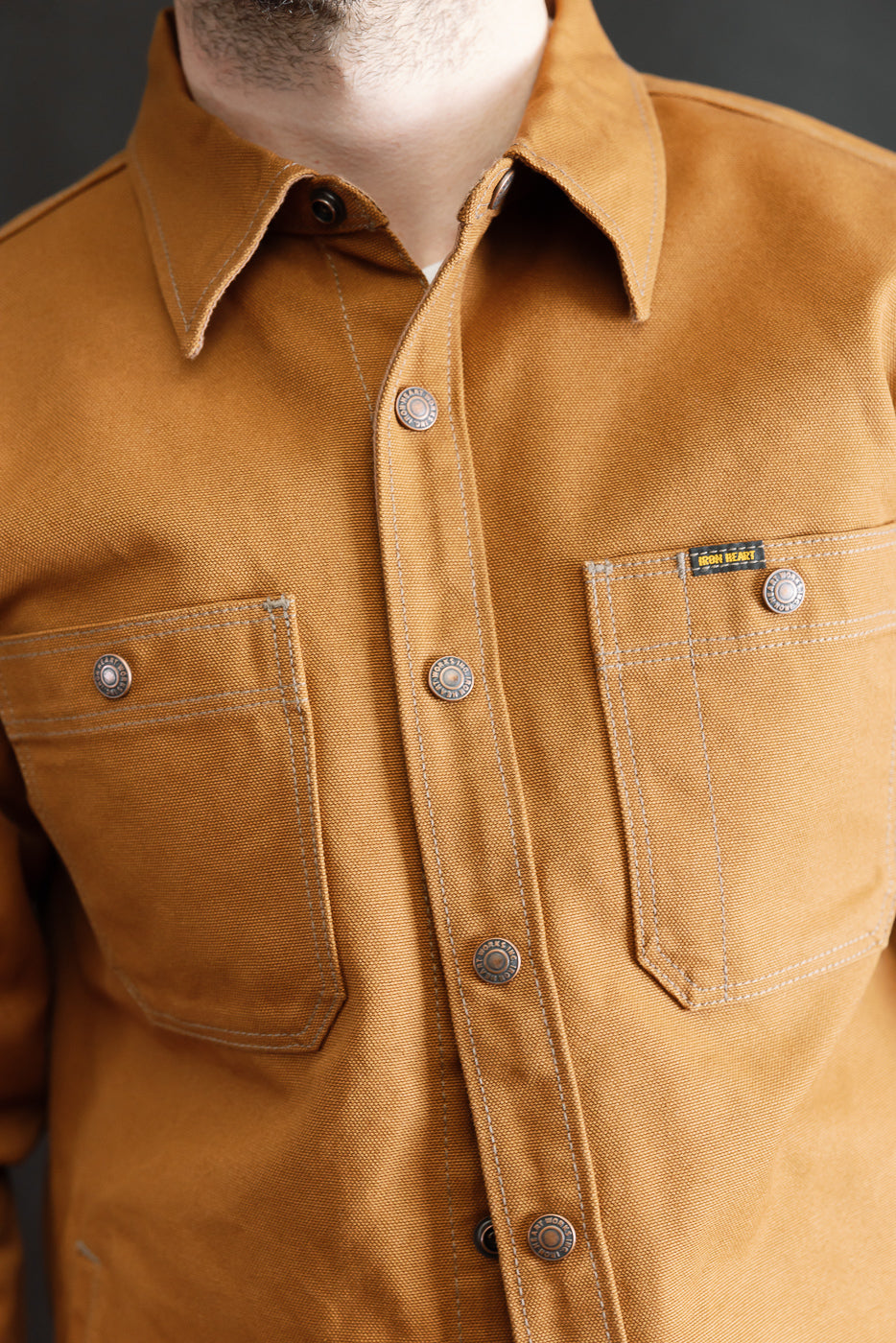 Close-up of front chest area of brown work shirt on male model, showing pockets, buttons, and collar.