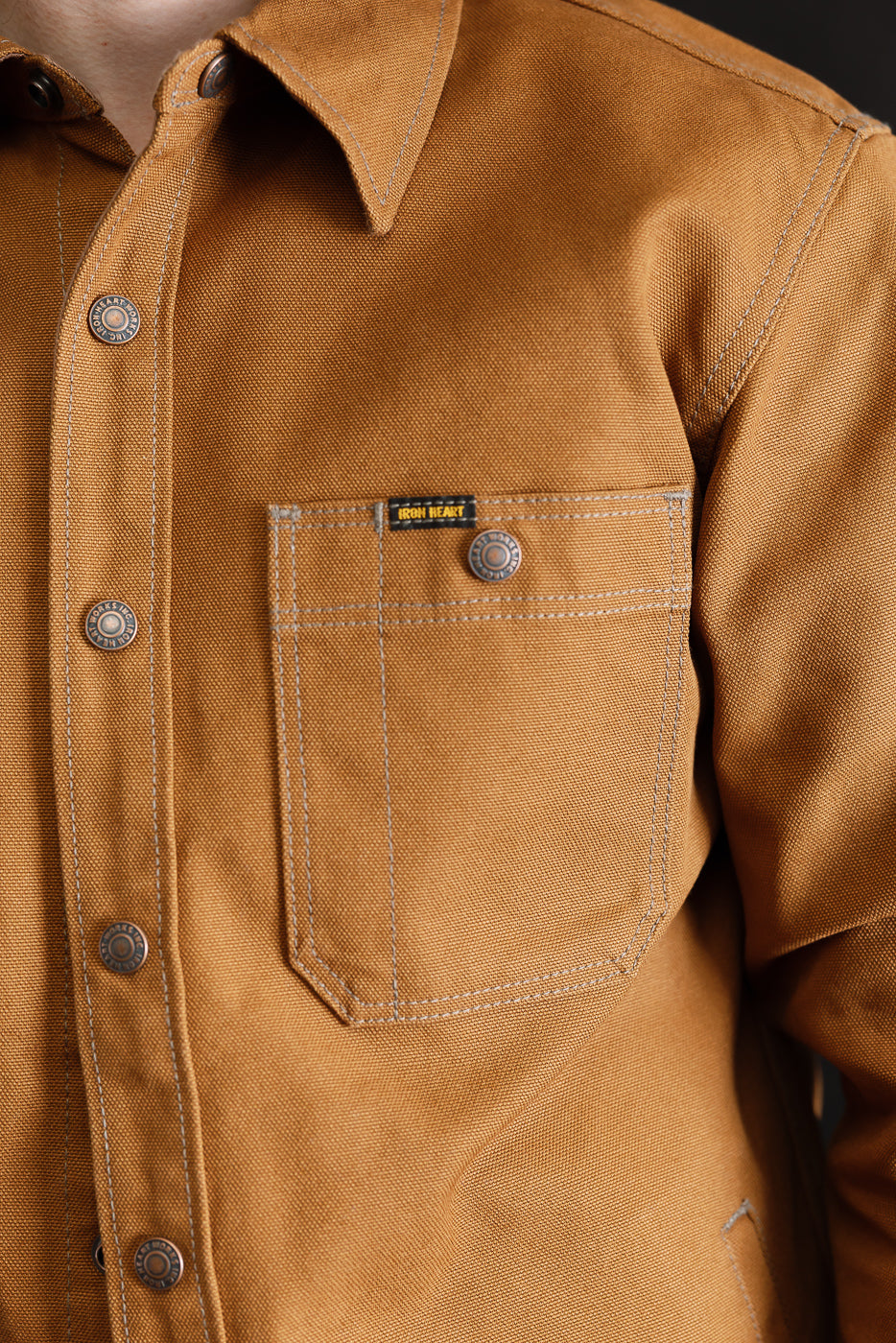 Close-up of male model wearing brown duck work shirt, front chest pocket and snap buttons visible.