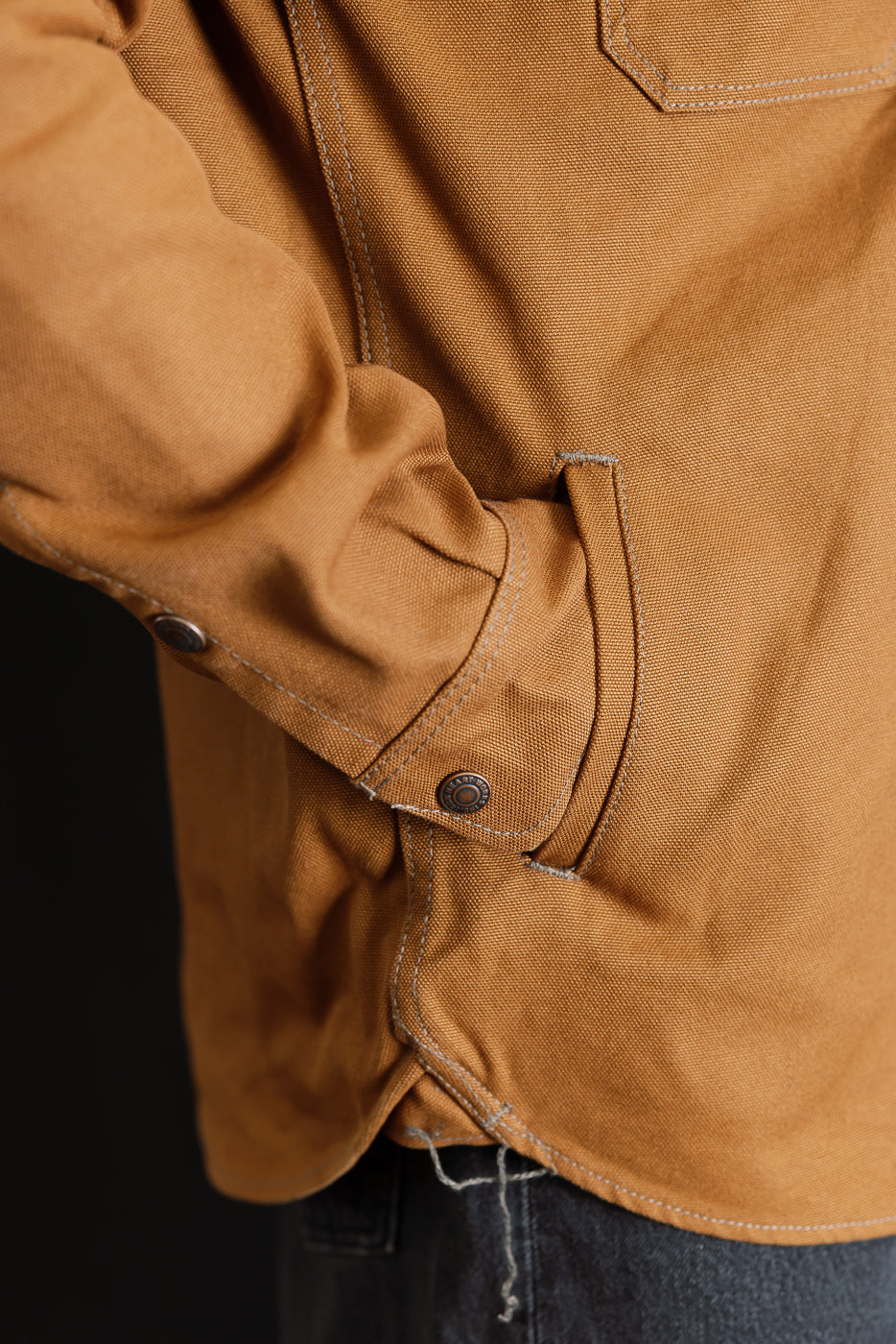 Close-up of male model wearing brown duck work shirt, showing side pocket, buttoned cuff, and heavy fabric texture.