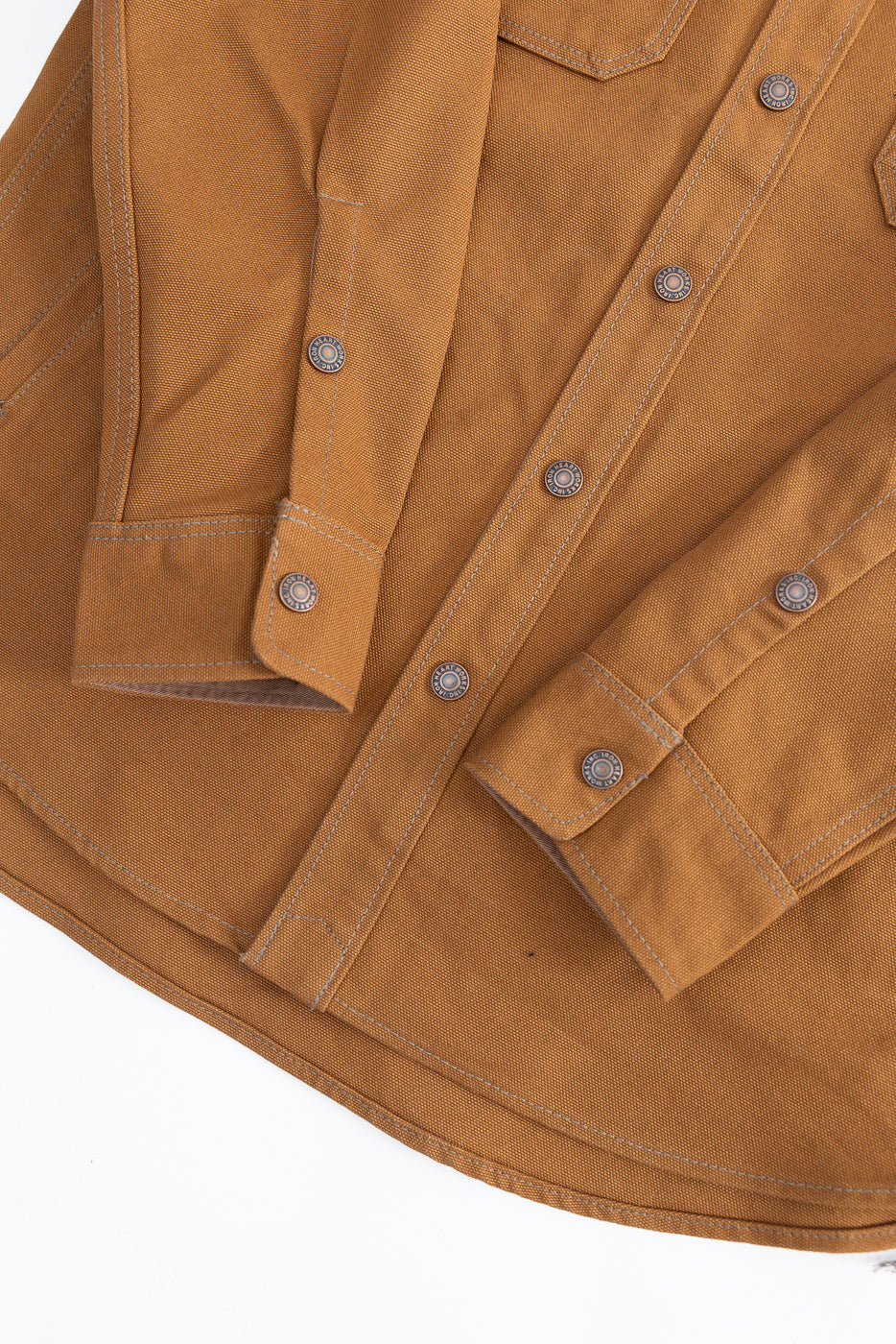 Close-up of brown duck work shirt front, showing snap buttons, cuff, and hem details.