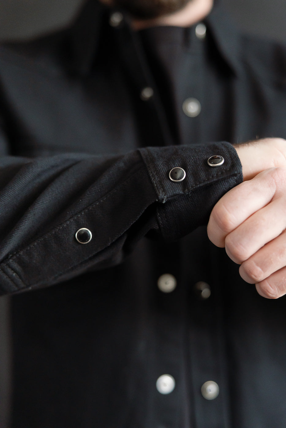 Close-up of Iron Heart IHSH-218 black selvedge denim western shirt cuff and snap buttons, on male model, athletic build, showing front sleeve details.