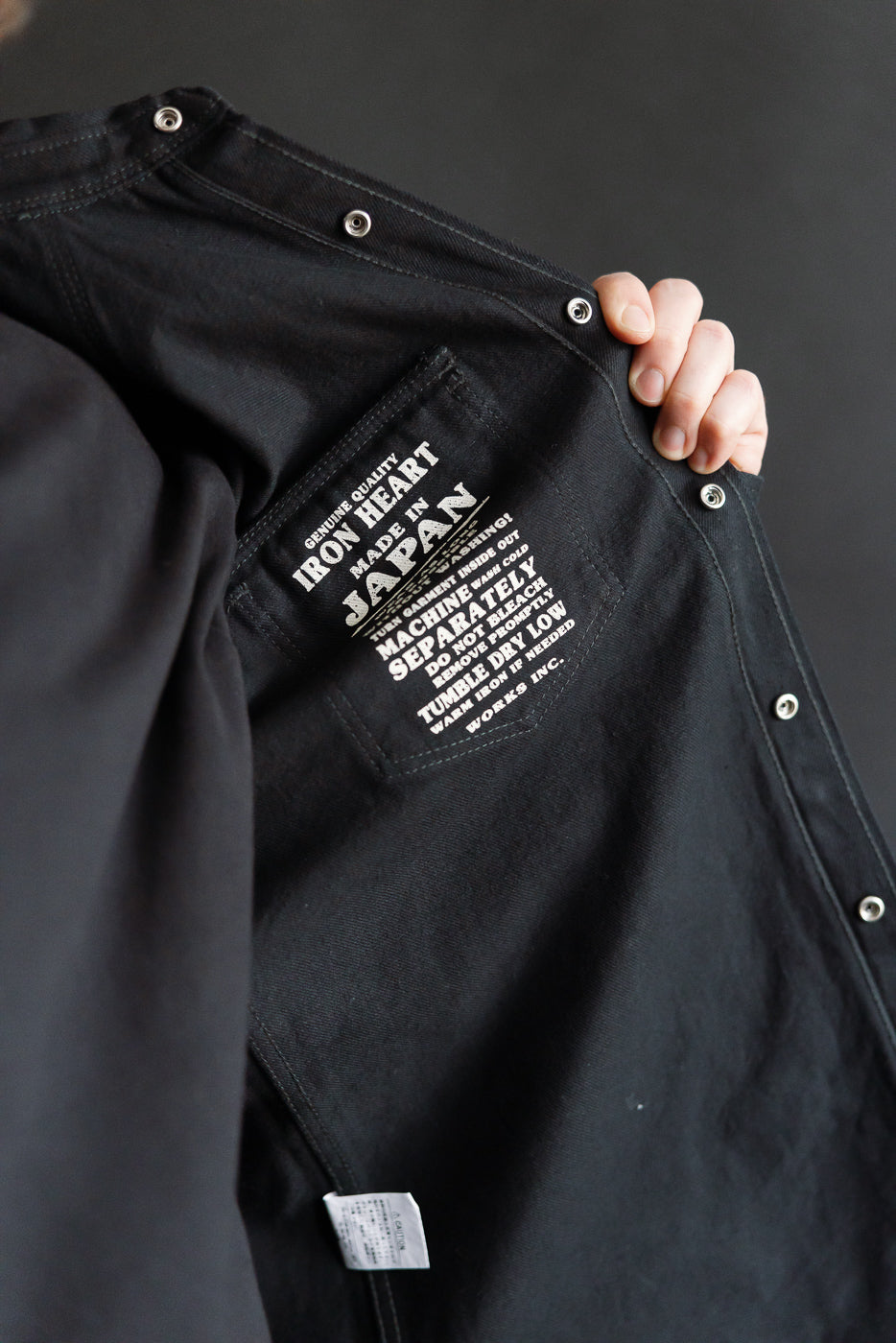 Close-up of Iron Heart IHSH-218 black 12oz selvedge denim western shirt interior label, left inside chest, showing snap buttons and care tag.