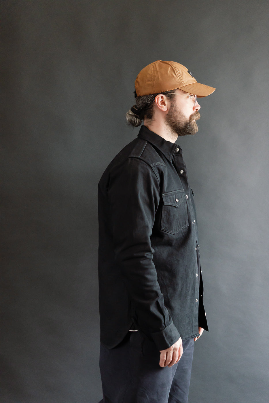 Male model 5'9 165lbs athletic build in black selvedge denim western shirt, side view