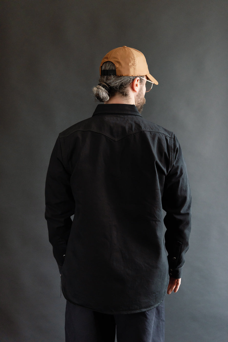 Male model 5'9 165lbs athletic build wearing Iron Heart black selvedge denim western shirt, back view, showing rear yoke and long sleeves.