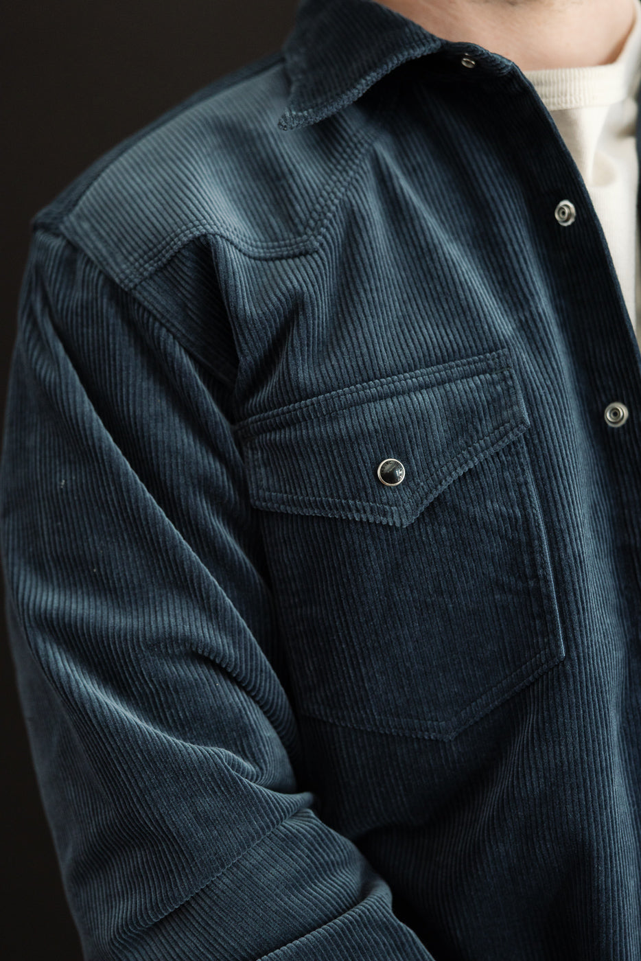 Close-up of men's navy corduroy western shirt front, left chest pocket, snap button, collar detail. Model is male, 5'9