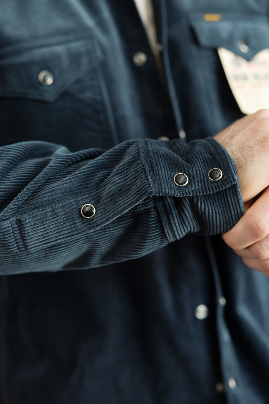 Close-up of men's navy corduroy western shirt front, showing sleeve cuff snaps and chest pocket, modeled by a male, 5'9
