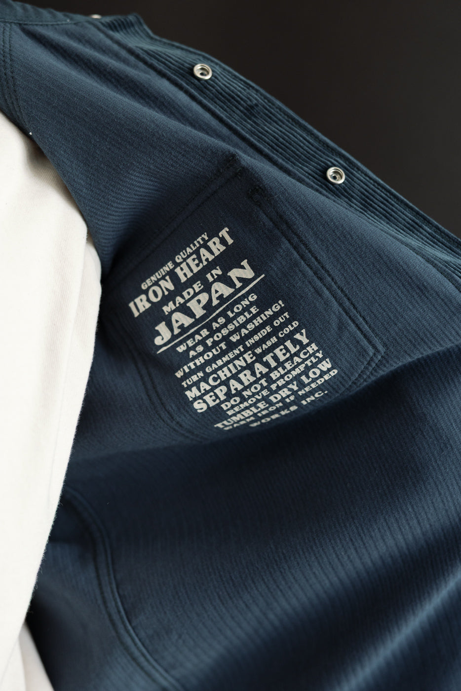 Close-up of navy corduroy jacket interior, showing 'Iron Heart Made in Japan' tag and care instructions, front view