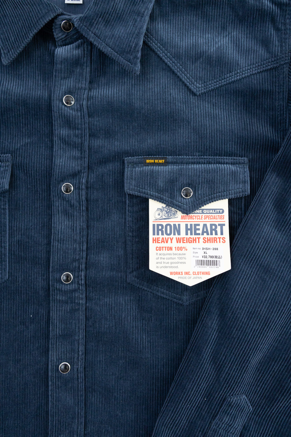 Close-up front view of navy corduroy western shirt chest, showing snap buttons, pointed collar, textured fabric, and branded chest pocket with hang tag.