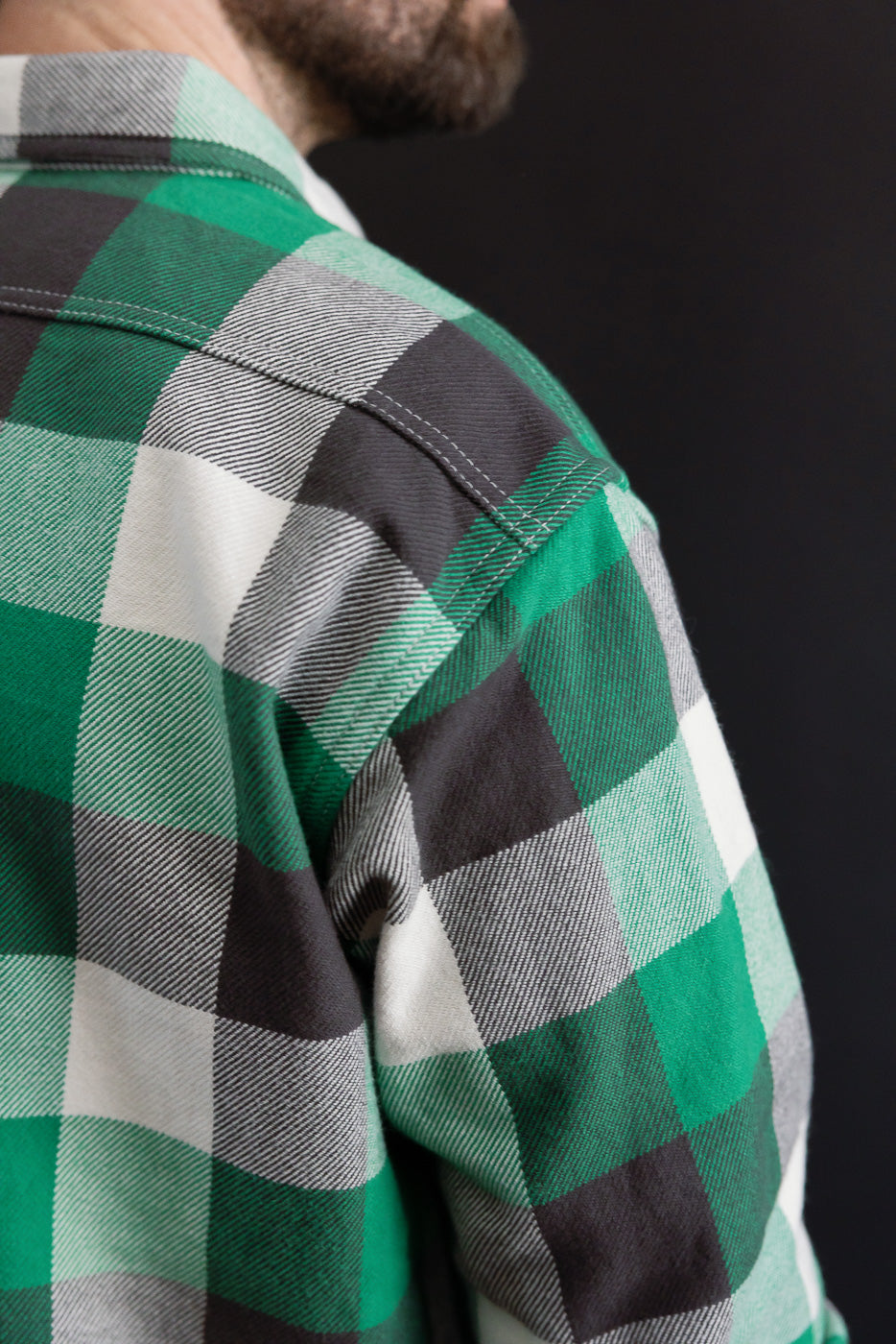 Close-up of male model's upper back and shoulder in Iron Heart IHSH-428-GRN ultra heavy green flannel shirt, showing yoke stitching and plaid fabric texture.