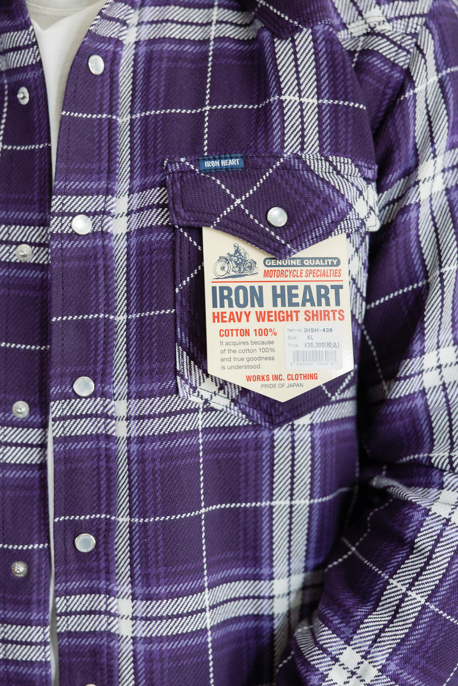 Close-up front view of purple plaid flannel shirt with chest pocket, tag, and silver buttons on male model