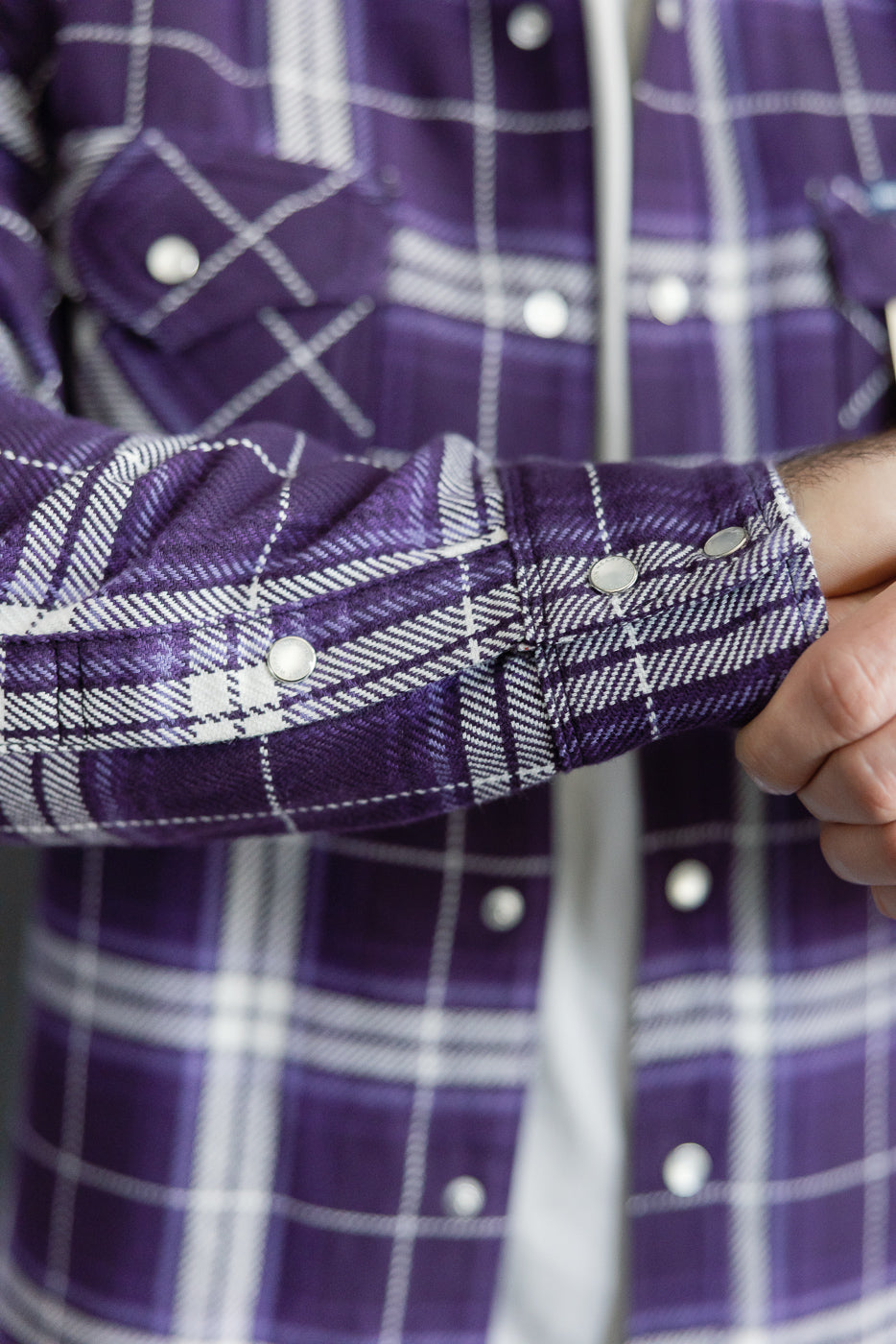 Close-up of male model's arm in purple plaid shirt, showing buttoned cuff and fabric texture
