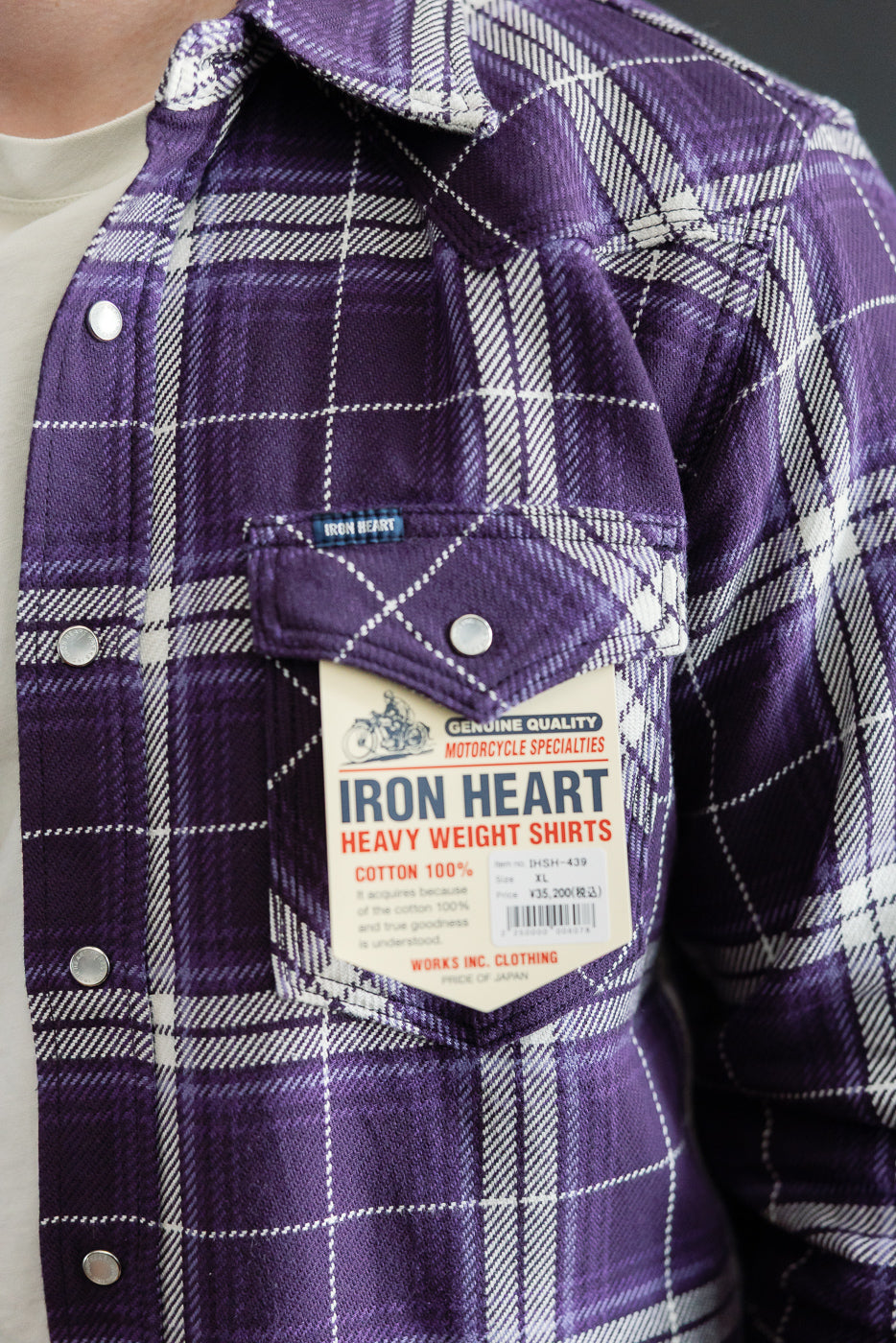 Close-up front view of male model wearing purple plaid flannel shirt with chest pocket, tag, and silver buttons