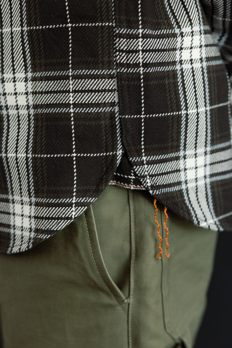 Close-up of black and white plaid flannel shirt hem, side view, showing fabric texture and orange side tag details.