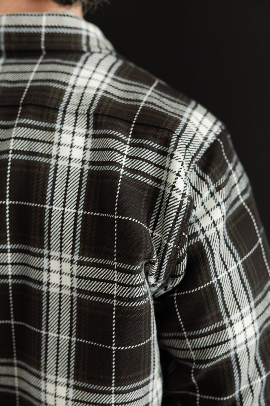 Close-up of male model's back wearing black and white plaid flannel shirt, showing fabric texture and yoke seam.