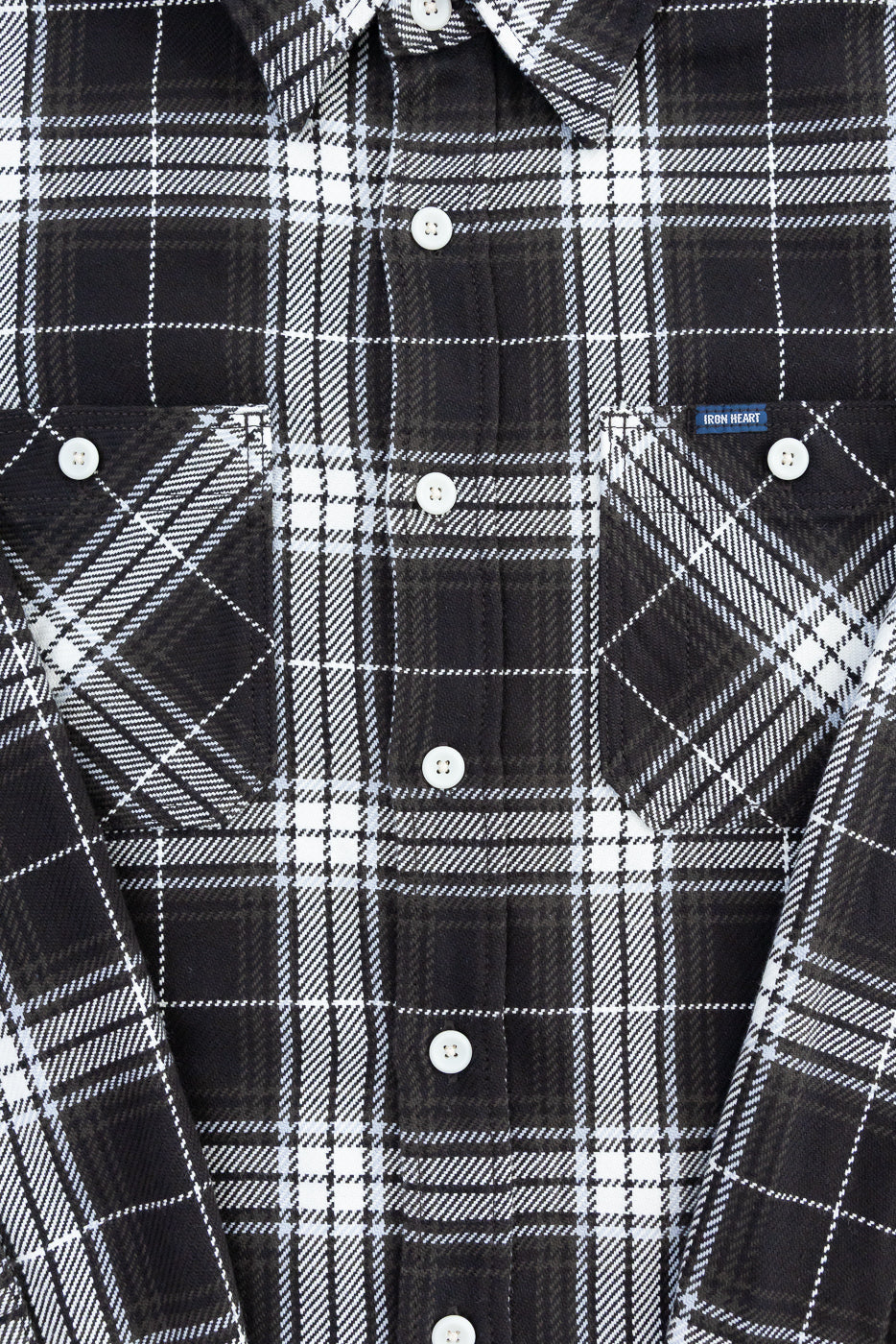 Close-up of front upper body of black and white selvedge flannel shirt, showing button-down pockets, white buttons, pointed collar, and plaid fabric texture.
