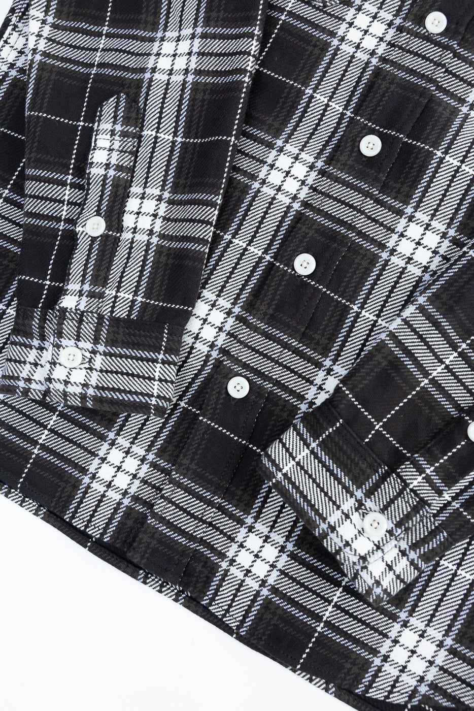 Close-up of front lower section of black selvedge flannel work shirt showing checked fabric, white buttons, and dual chest pockets.