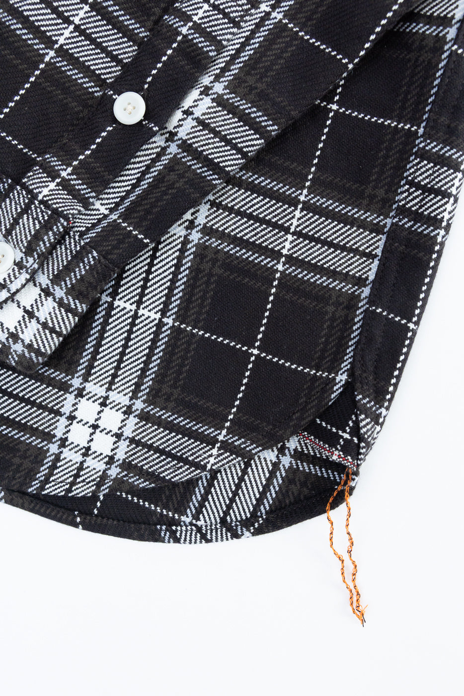 Close-up of front hem and lower button area on black plaid selvedge flannel work shirt, showing fabric texture and button detail.