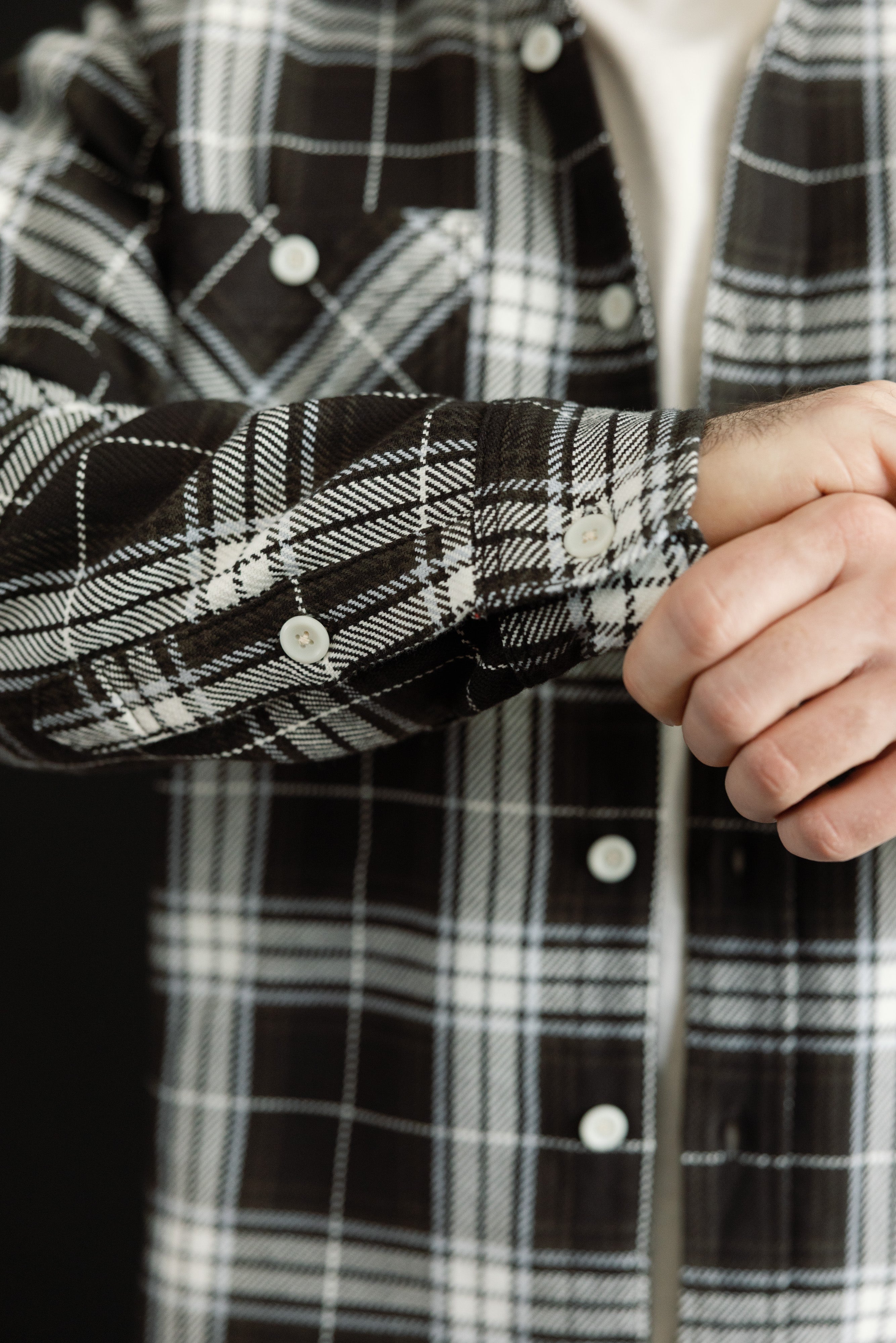 Close-up of male model's arm showing front left sleeve cuff, black and white plaid flannel shirt, pearl buttons, athletic build, 5'9