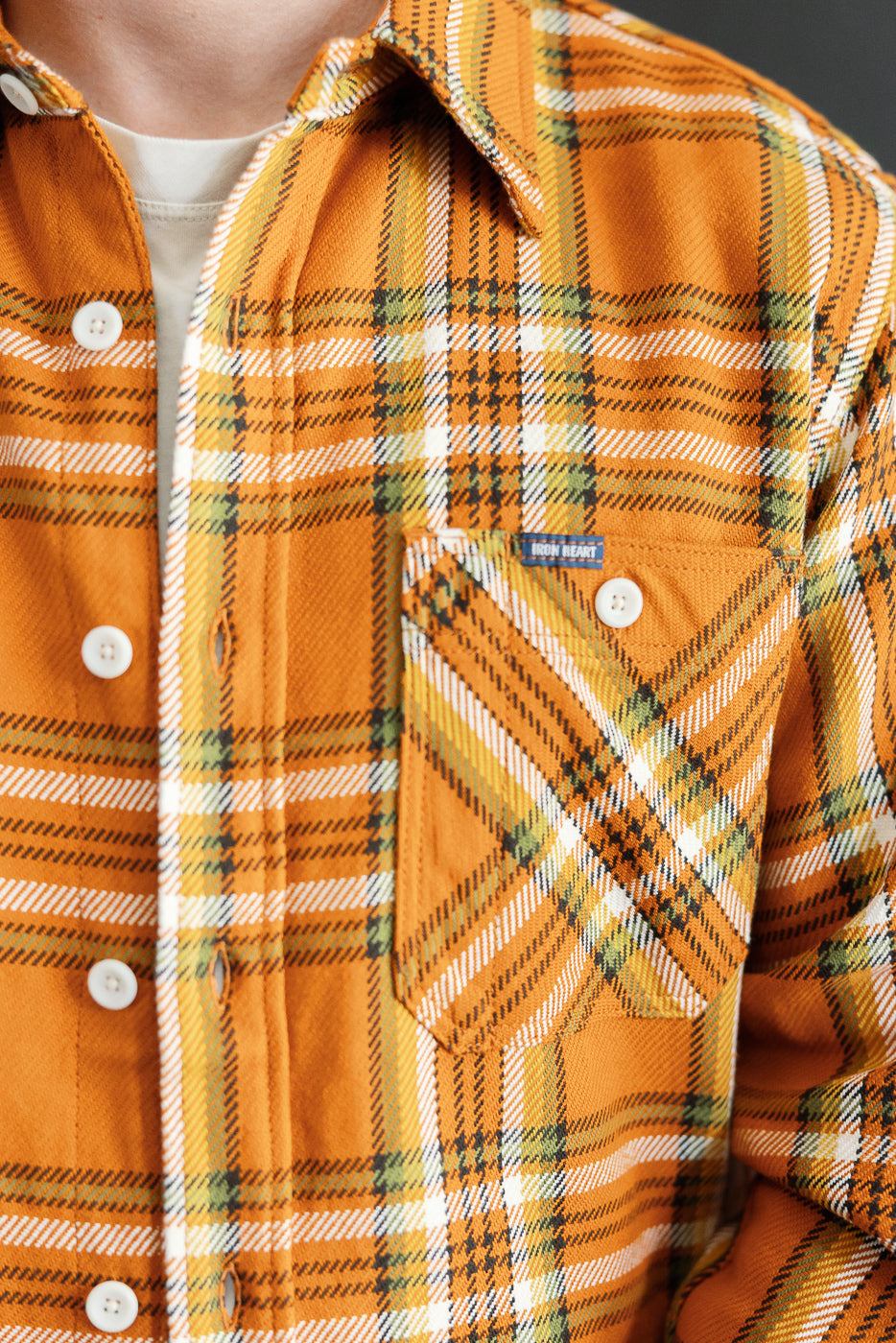 Close-up front view of male model in orange plaid shirt with white buttons and chest pocket tag