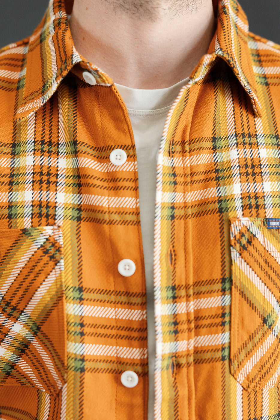 Close-up front view of male model wearing orange plaid shirt with white buttons and chest pocket