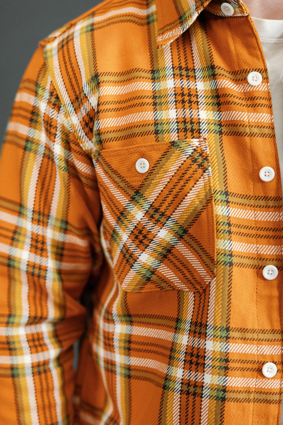 Close-up front view of orange plaid shirt with white buttons, chest pocket, and fabric texture on male model.